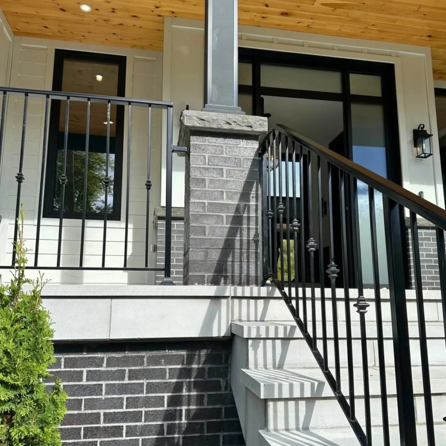 House entrance with brick and stone columns, a timber canopy and dark railings