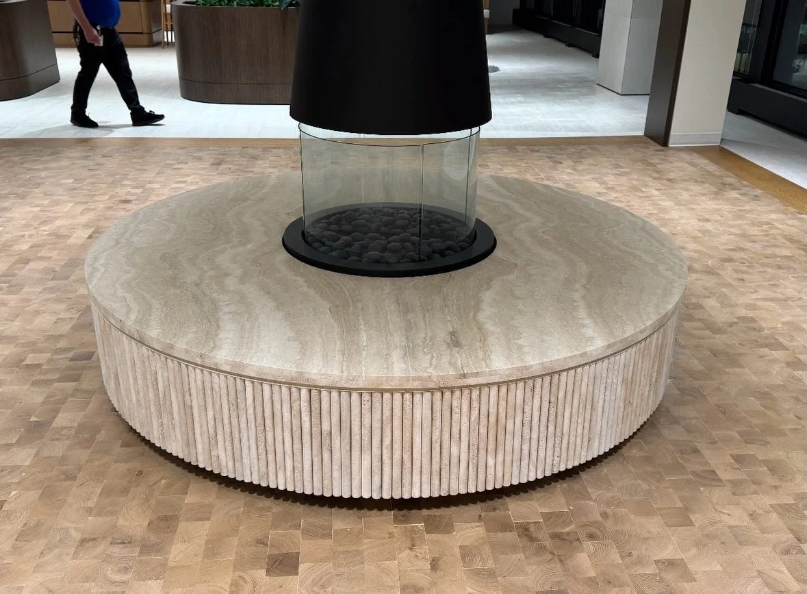 Circular stone bench with a fluted outer edge surrounding a central suspended fireplace
