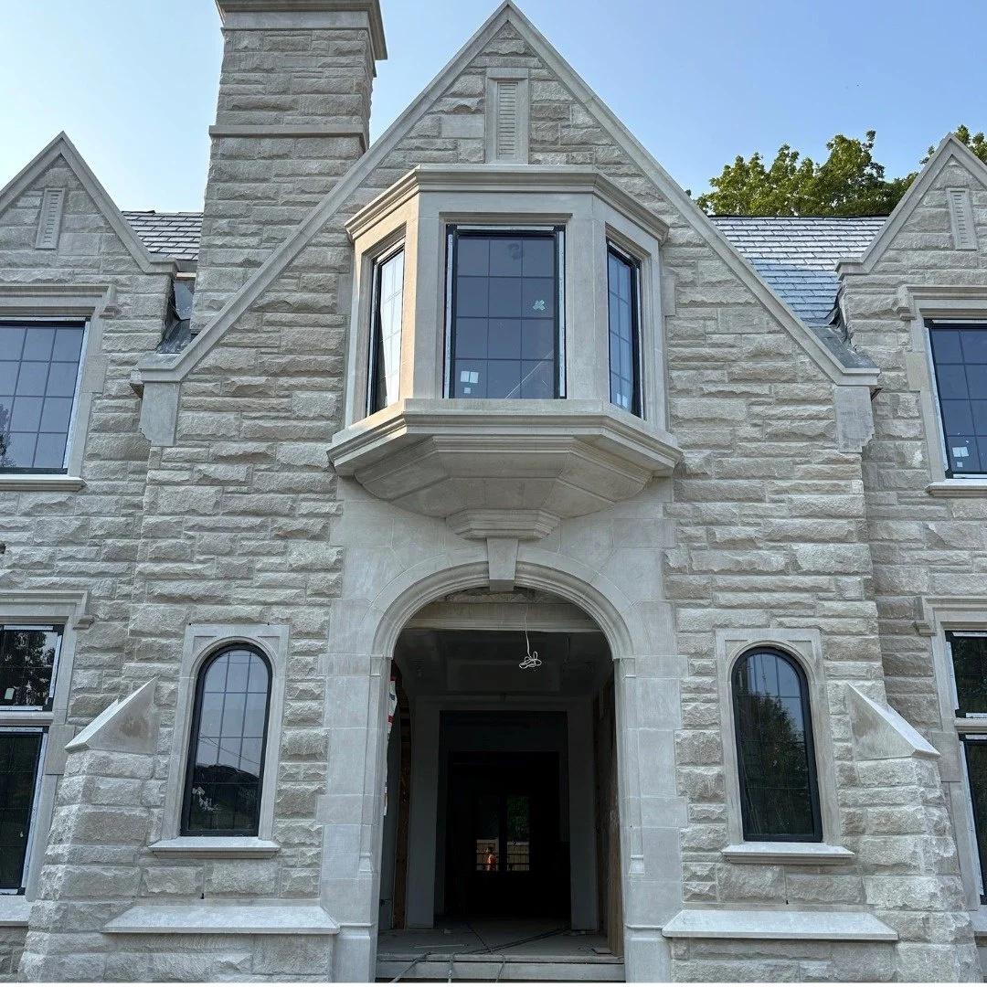 Grand arched limestone entrance and upper bay window with detailed cut-stone profiles