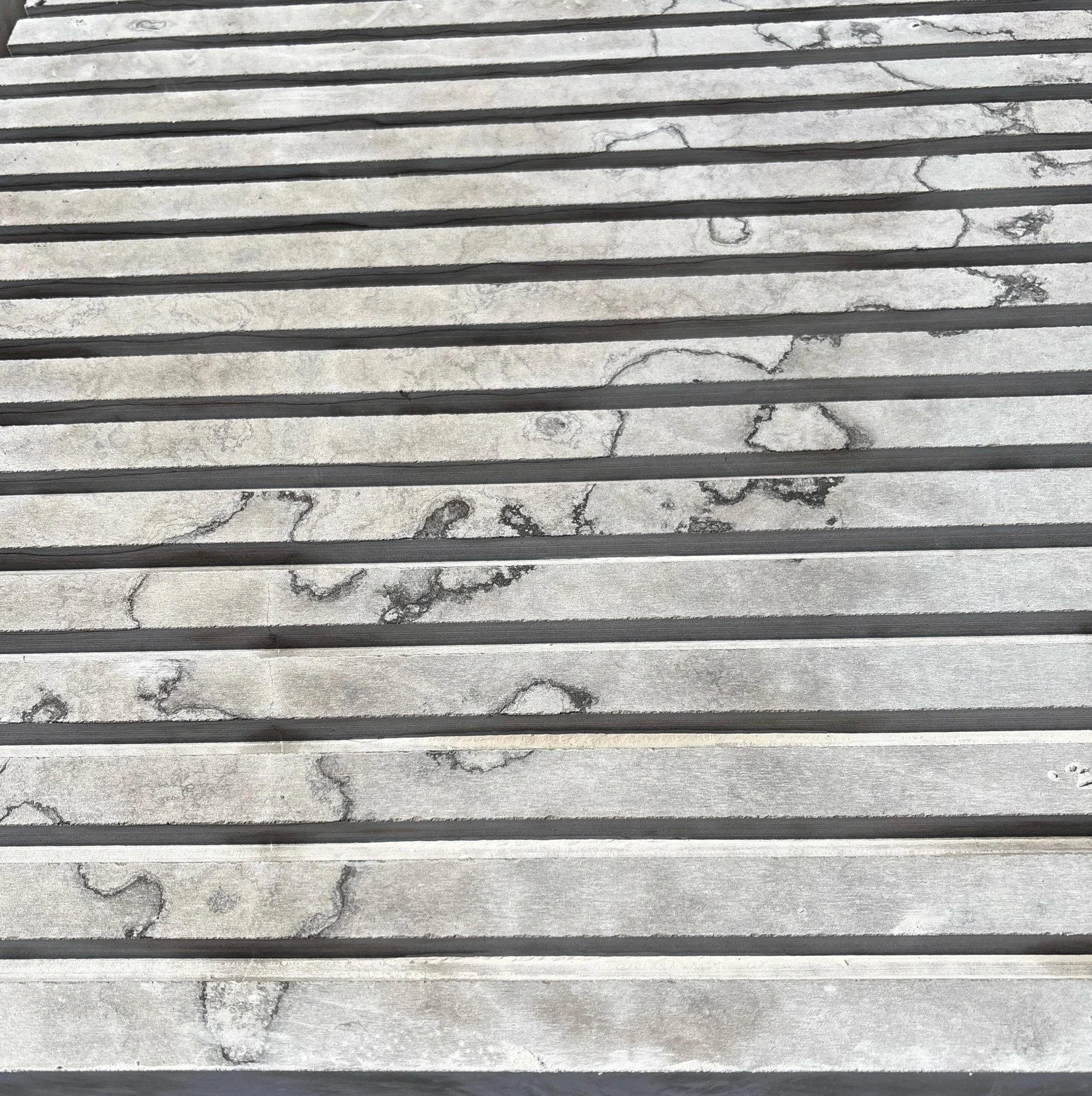 Parallel flutes cut into a natural stone surface, showing veining and a custom profile