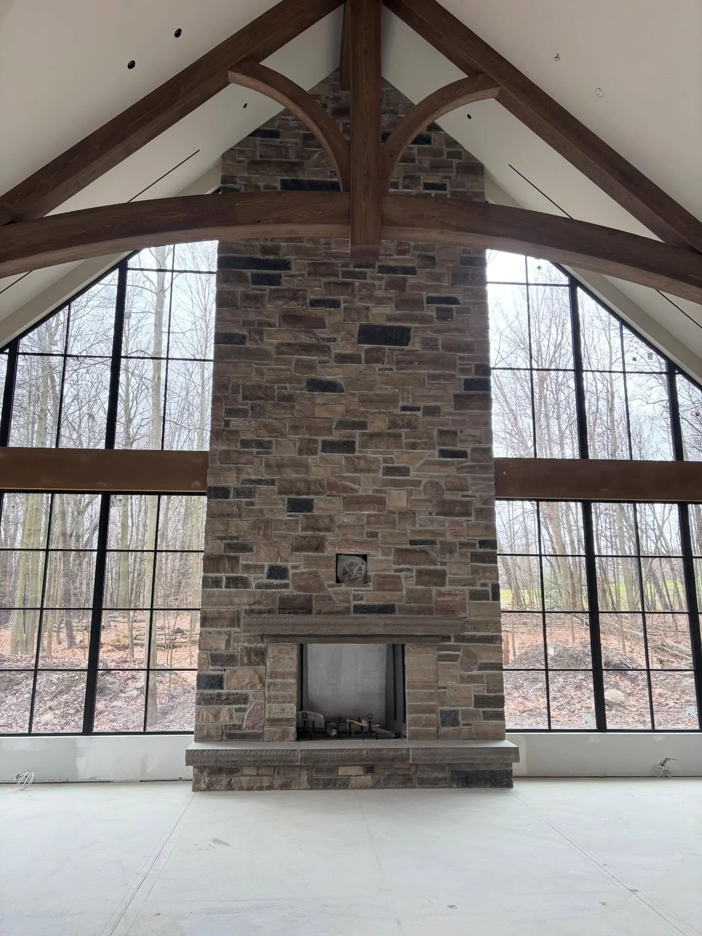 Floor-to-ceiling stone fireplace framed by large windows and exposed timber roof beams