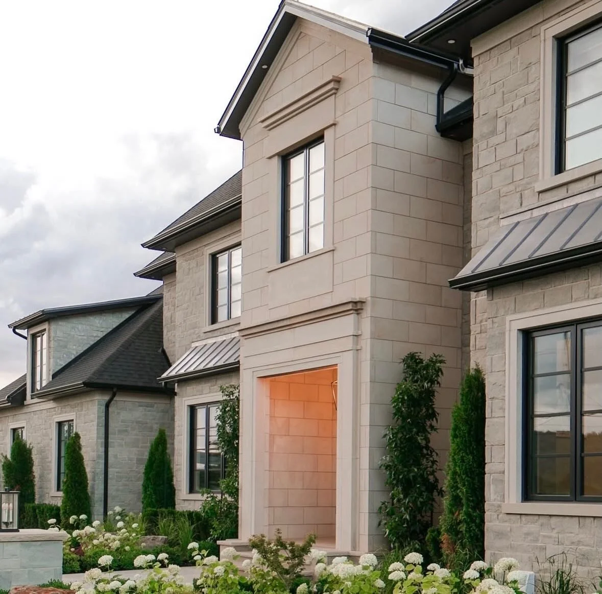 Pale stone-clad townhouse with recessed entrance, dark windows and clipped planting
