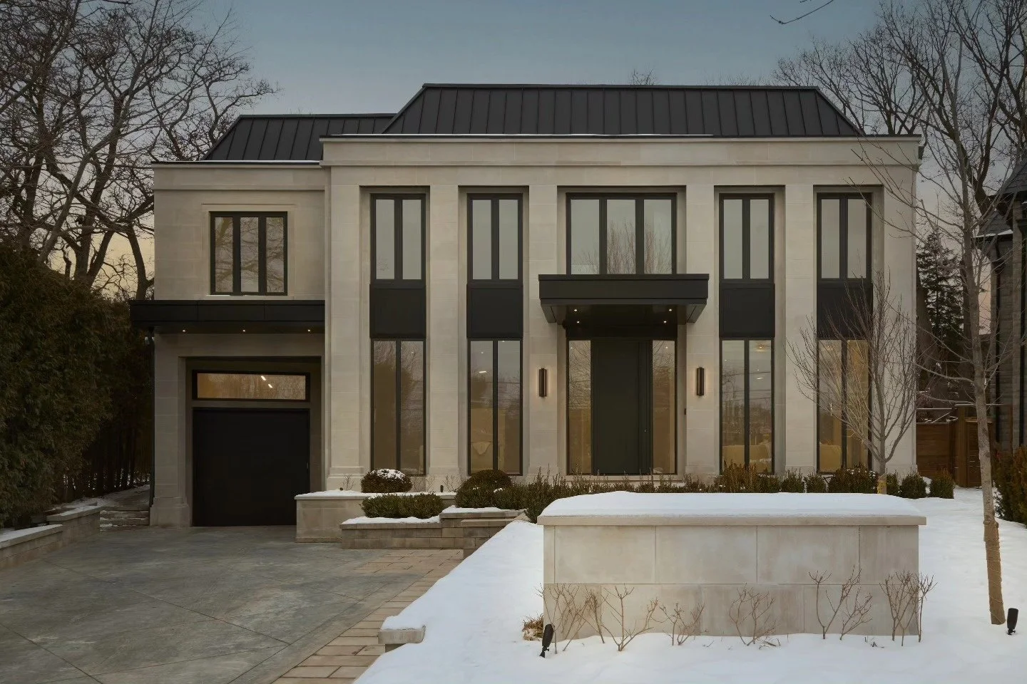 Symmetrical modern pale stone house with dark windows and a snow-covered foreground
