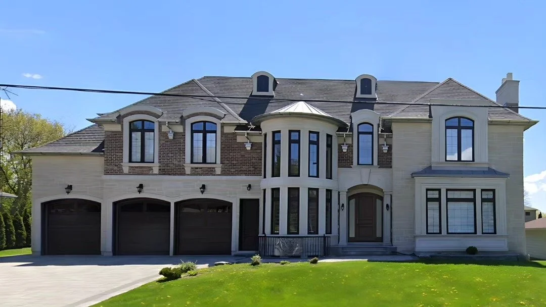 Wide front elevation of a large pale stone home with garages and arched entrance